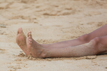 A person's feet are laying in the sand on a beach