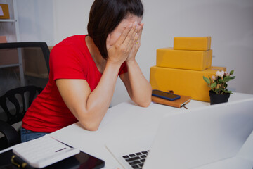 An Asian woman in a light red T-shirt is selling goods online, efficiently packing orders for...