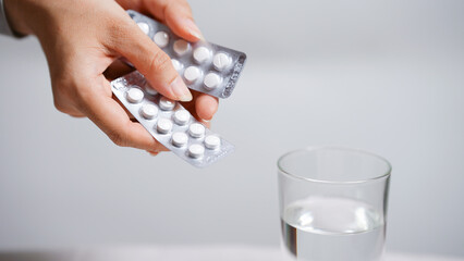 Hand holding pill blister packs with a glass of water