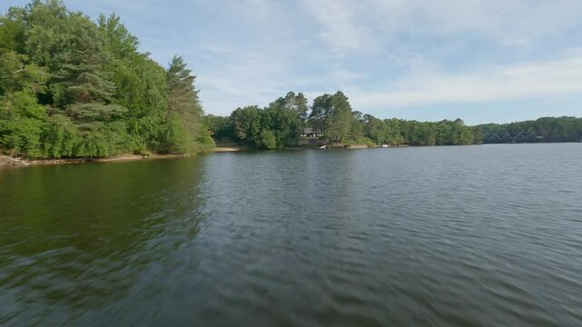 Aerial view FPV drone flies low along forested lake shore towards Pont de Lantourne, Marcillac La Croisille, France