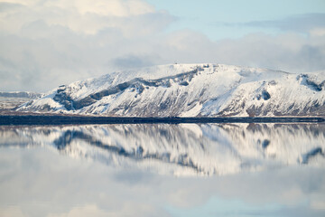 Snowy mountain reflecting in calm water in iceland under cloudy sky