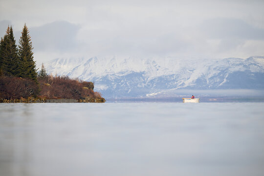 Fisherman rowing on a calm lake with snowy mountains