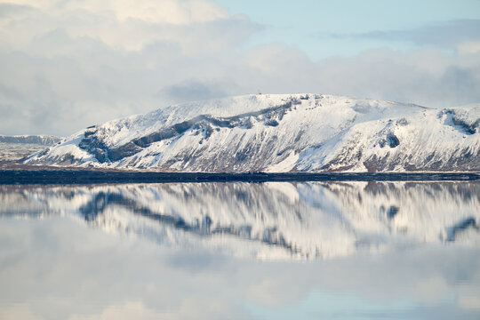 Snowy mountain reflecting in calm water in iceland under cloudy sky