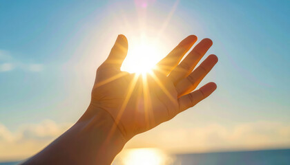 Hand reaches toward bright sunlight, creating inspirational and hopeful mood against clear blue sky