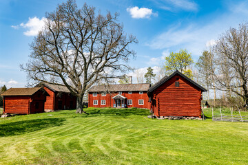A typically red wooden house and barn in a Swedish summer landscape