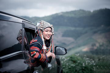 Happy woman dressed in traditional tribal out of the window of a car enjoying the fresh mountain air green hills mist-covered valleys stretch out in the background.