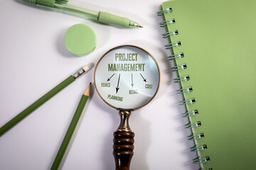 Project Management Concept Under Magnifying Glass with Office Supplies on White Background