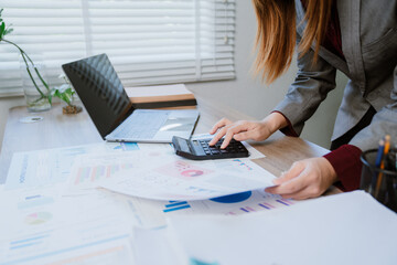 Young happy asian businesswoman using calculator and smartphone calculating financial data working...