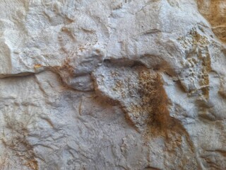 Detailed view of a rugged rock face with uneven texture, featuring light brown and gray hues,...