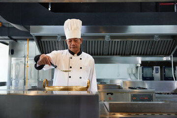 senior chef cooking some food and preparing soup in the kitchen