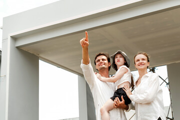 Smiling family pointing and admiring their future home construction site, symbolizing new beginnings, real estate investment, home ownership dreams, and residential development lifestyle.