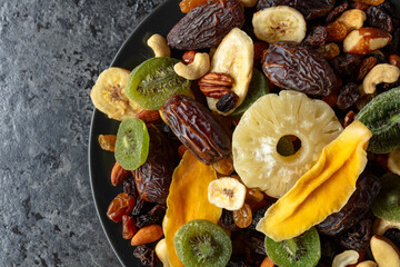Dried tropical fruits, nuts, and raisins in black plate.