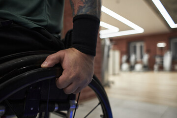 Obraz premium Close-up of tattooed arm resting on wheelchair handle with modern gym equipment blurred in background suggesting active and accessible fitness environment