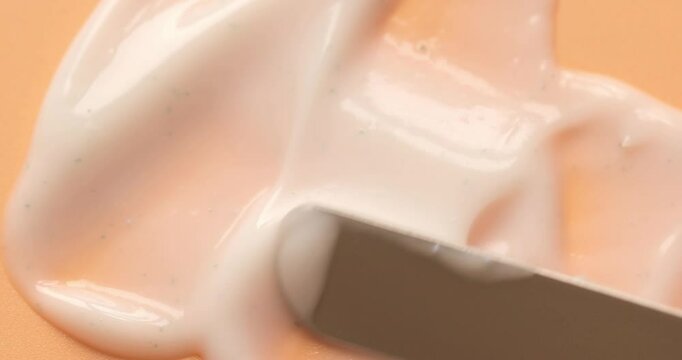 Making skincare cosmetic product smears with metal spatula on beige background close up. Beauty abstract	