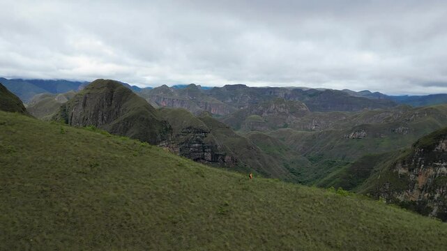 Aerial pulls back as hiker jogs down mountain ridge, Codo de los Andes