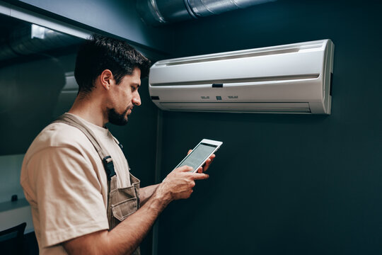 Technician checks air conditioning unit using tablet in modern indoor setting during day