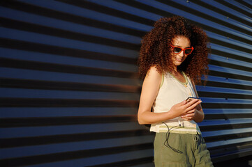 stylish woman with smartphone smiling outdoors in sunlight. modern urban lifestyle depicted with...