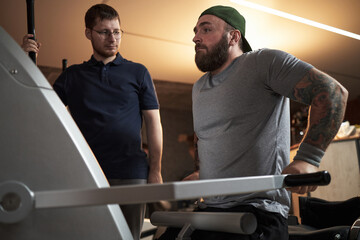Fitness trainer monitoring workout routine at gym with focused expression, guiding the session and...