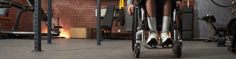 Header with individual working out in gym using wheelchair. Various fitness equipment, including...