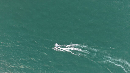 Aerial view of a personal watercraft creating a wake on a beautiful turquoise ocean surface, capturing the thrill and freedom of water sports