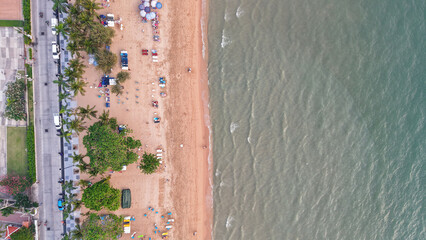 Tourists relaxing on beach chairs and colorful umbrellas dot the sandy shore, while gentle waves lap at the coastline in this inviting aerial view of a tropical paradise