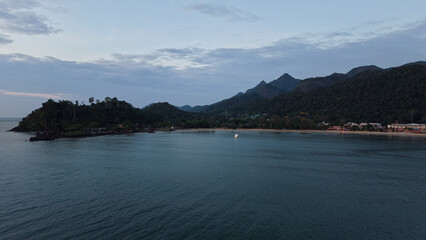 Calm ocean waters reflecting the warm hues of sunset light, framed by majestic mountains and a pristine beach, creating a tranquil and serene atmosphere perfect for relaxation