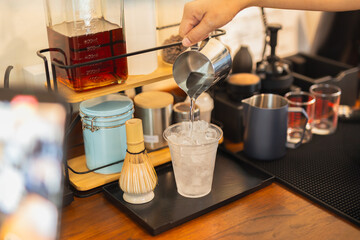 Barista hand pouring water from pitcher in to a glass with iced.