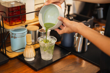 Woman barista pouring matcha green tea into a glass with water.