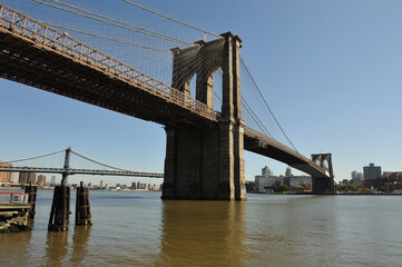 The iconic Brooklyn Bridge stretches majestically over the East River, connecting Manhattan and Brooklyn against a backdrop of clear blue sky