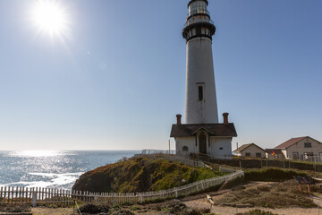 Fototapeta premium A classic California lighthouse stands majestically on rugged cliffs above the Pacific Ocean, bathed in bright sunlight