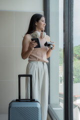 Young woman tourist holding United States passport, dollars and camera looking out window while...