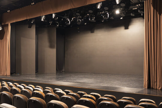 Empty theater stage with curtains, auditorium seating, and overhead spotlights, ready for a performance or presentation, wide interior with copy space.