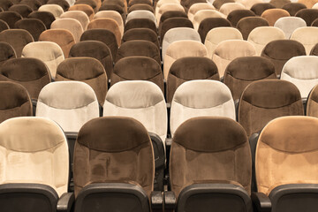 Naklejka premium Rows of empty auditorium chairs in soft neutral tones, creating a symmetrical pattern ideal for concepts of events, gatherings, or public spaces.