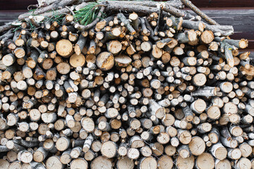 Stack of firewood and branches neatly arranged against a wooden log cabin wall, natural background