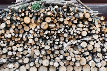 Selbstklebende Fototapeten Stack of firewood and branches neatly arranged against a wooden log cabin wall, natural background © Irina