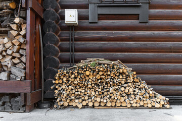 Stack of firewood and branches neatly arranged against a wooden log cabin wall, with rustic and...
