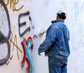 Painter covering graffiti on a public building wall with white paint