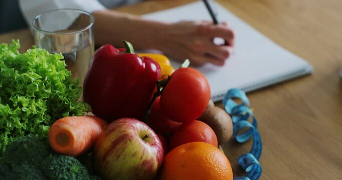 Close up of nutritionist woman writing diet plan on table full of fruits and vegetables. Healthy nutrition, eco food.