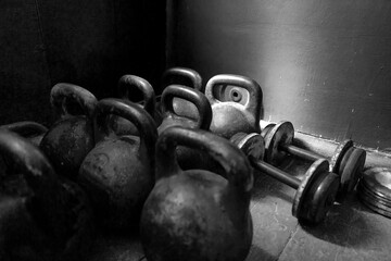 A collection of vintage 24 kg kettlebells and dumbbells in a corner, showcasing their worn texture...