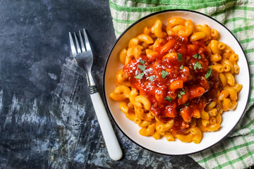 a plate of macaroni bolognese pasta and a fork, on a black background with negative space