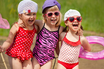 Little girls in bathing suits have fun during summer time on the lake beach.