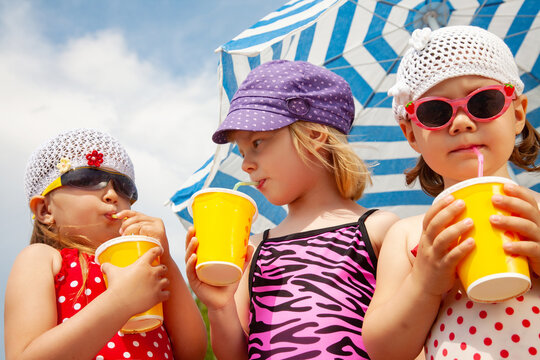 Little girls in bathing suits drinking sweet drinks from a straw under a sun umbrella