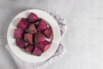 Top view of sliced Okinawan sweet potato on white plate against gray background. Vibrant purple root photographed in minimalist setting suits healthy food visuals and clean eating campaigns
