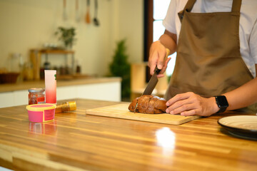 Man preparing breakfast by slicing loaf of bread, with ingredients arranged on a wooden countertop