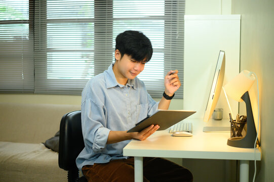Smiling asian entrepreneur working from home and reviewing documents at a desk