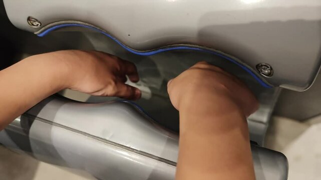 Hands drying under an electric hand dryer in a public restroom