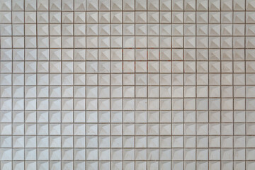 A frontal view of a wall covered with small square tiles, each featuring a raised pyramid shape....