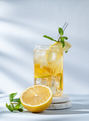 Iced drink with lemon and mint in a glass on a marble stand on light background with sunlight