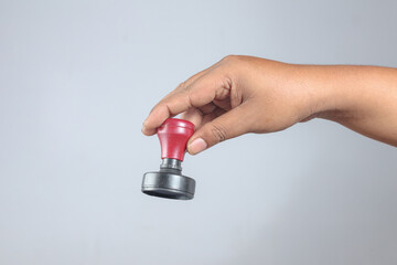 Hand holding round red and black rubber stamp showing office tool used for document authorization, verification, or approval process