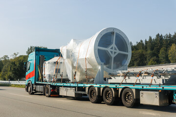 Long heavy industrial truck semi trailer platform transport disassembled wind turbine component wrapped plastic common highway on bright summer day. Energy industry equipment transportation service